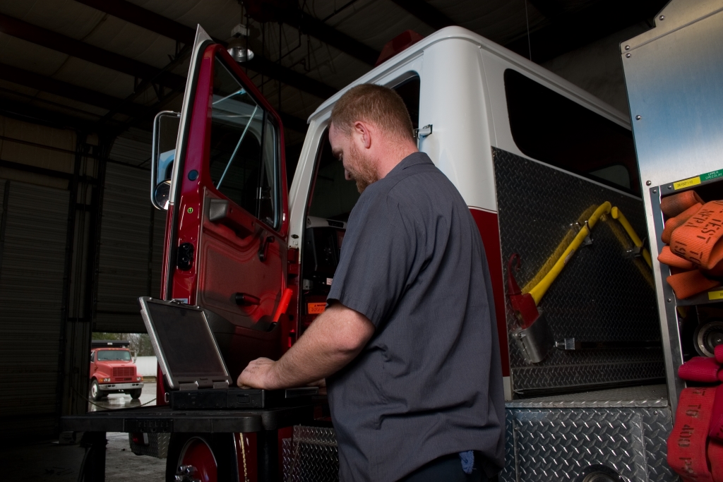 Technician using a diagnostic laptop beside a truck in a workshop